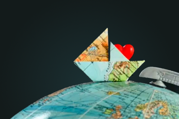 paper map origami sailboat with a red paper heart inside  placed on top of a globe