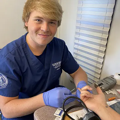 A nursing student smiles while taking a patient's blood sugar.