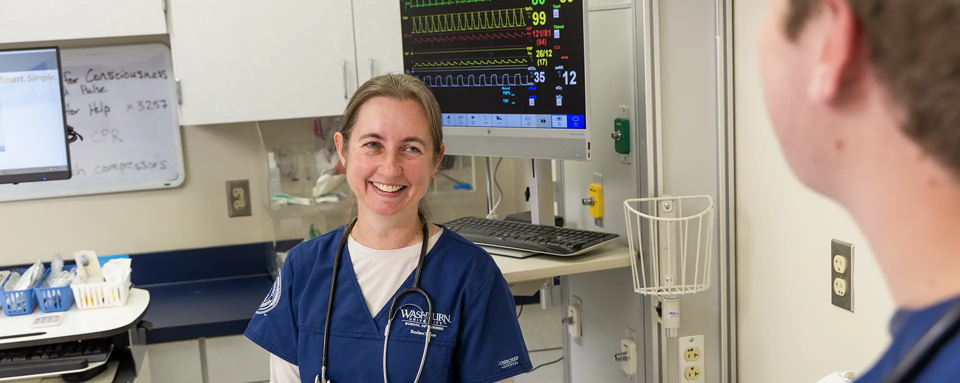 A nursing student smiles while learning in a simulation lab.