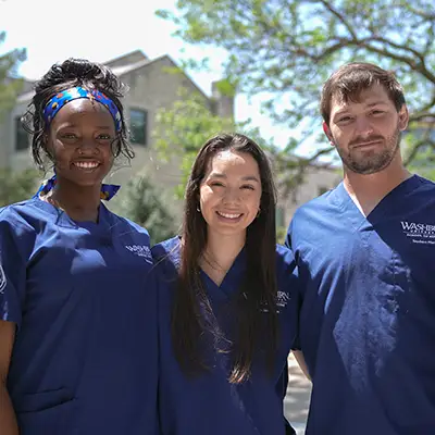 Nursing students wearing Washburn blue scrubs smiling.