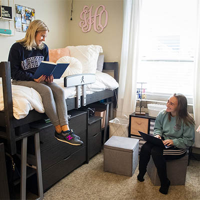 Two students smile while studying in their dorm room.