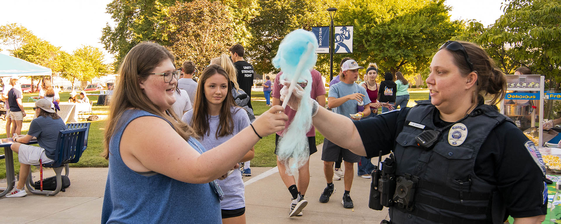 A police officer hands out cotton candy at a student event.