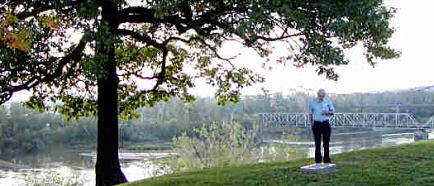 Max stands on hillside. Behind him is the Missouri River and the Amelia Earhart bridge